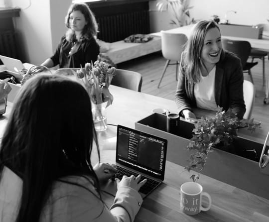 Women sitting in front of computers in a cozy workspace.